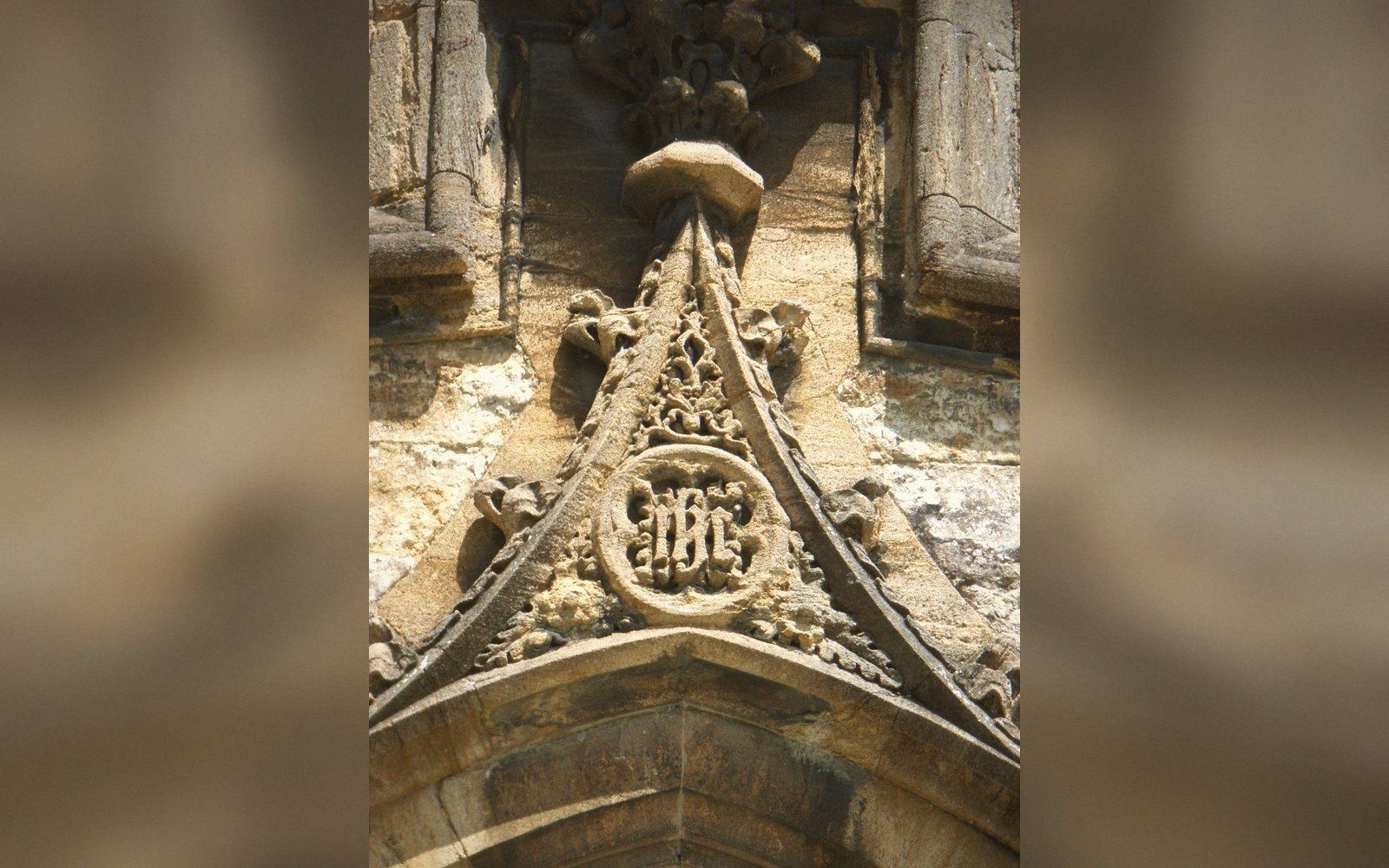 Carved stone gable with a monogram medallion above a church doorway arch