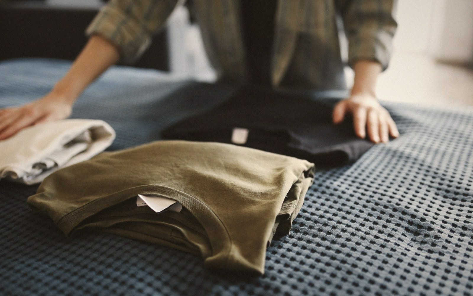 Person folding neatly stacked shirts on a textured blue bedspread
