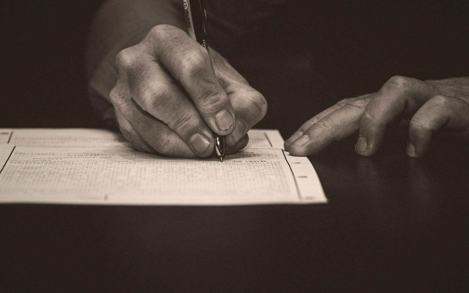Close-up of hands writing with a pen on a densely printed document