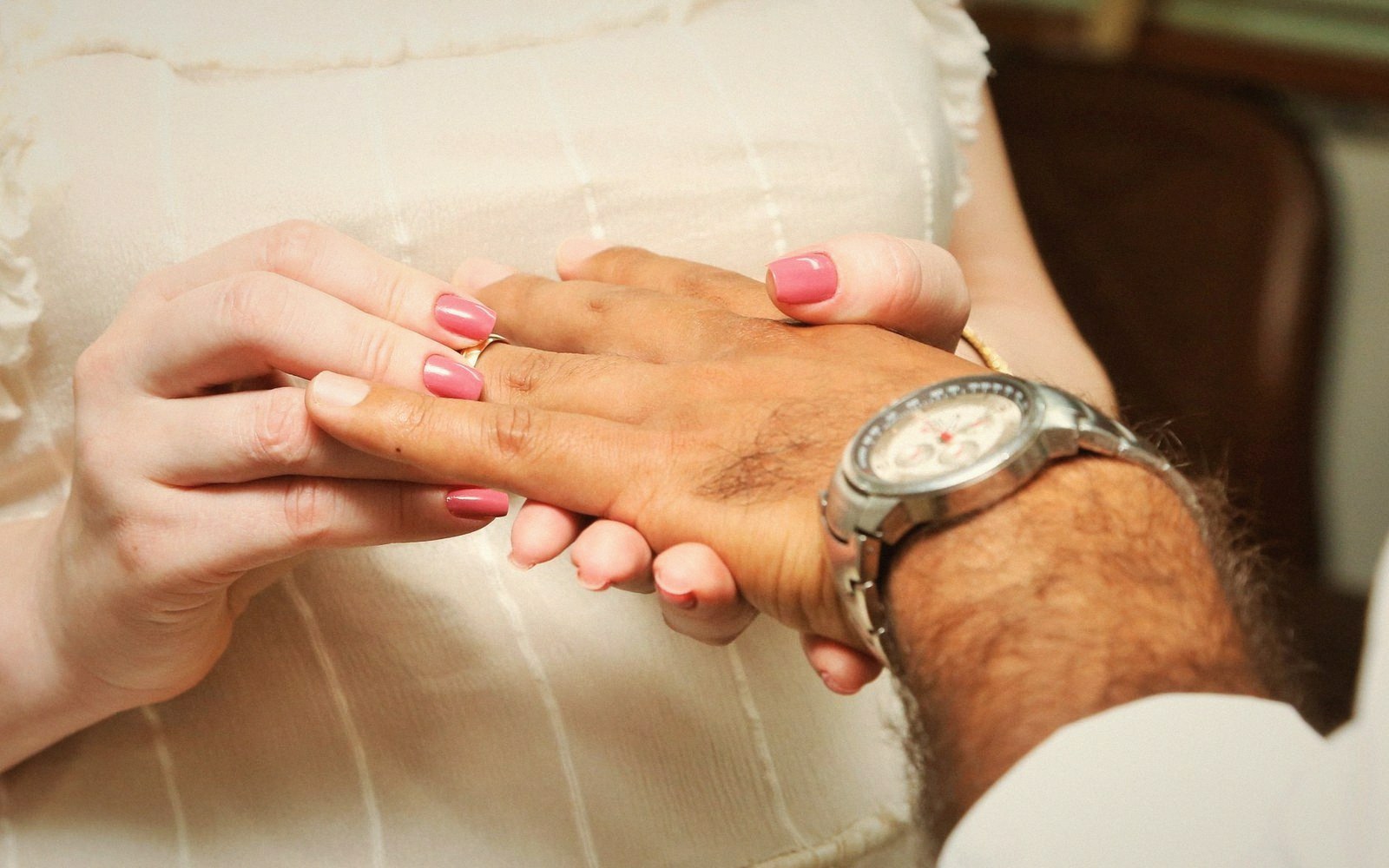 A woman places a wedding ring on a man's finger, his other wrist wearing a watch