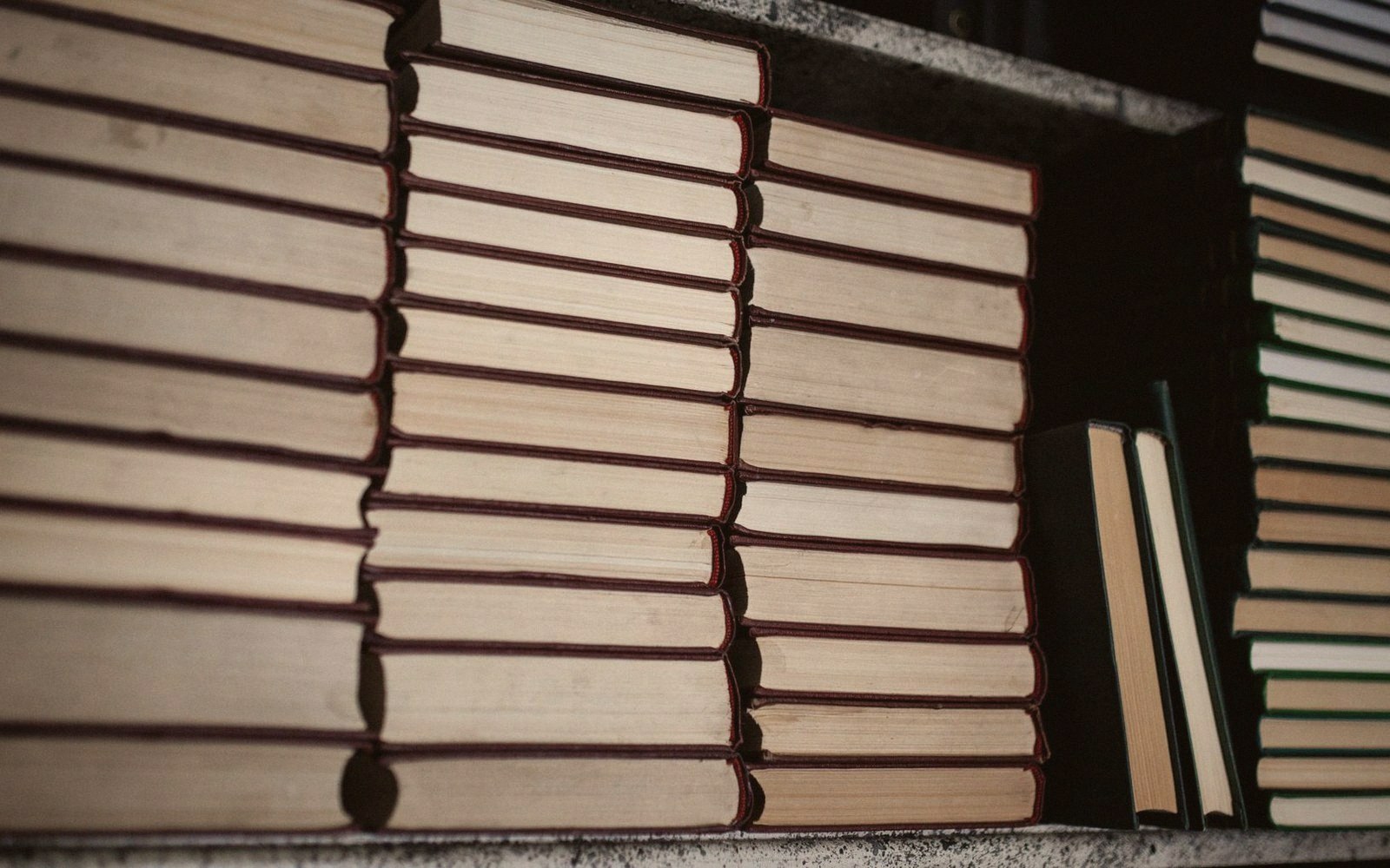 Stacks of hardcover books lying flat, showing their pages, on a shelf