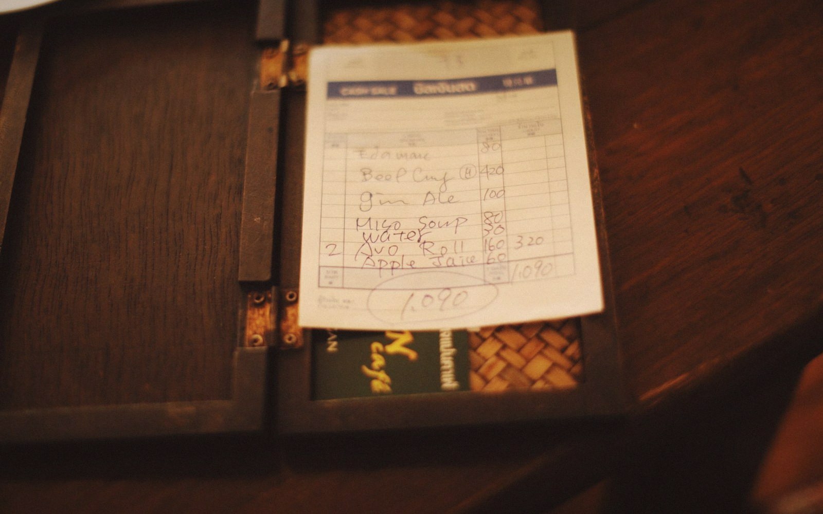 A handwritten cash sale receipt tucked inside a wooden bill folder on a table