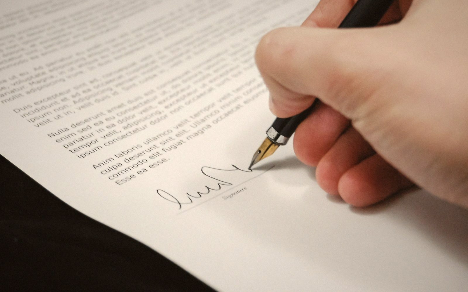 A hand uses a fountain pen to sign a printed document
