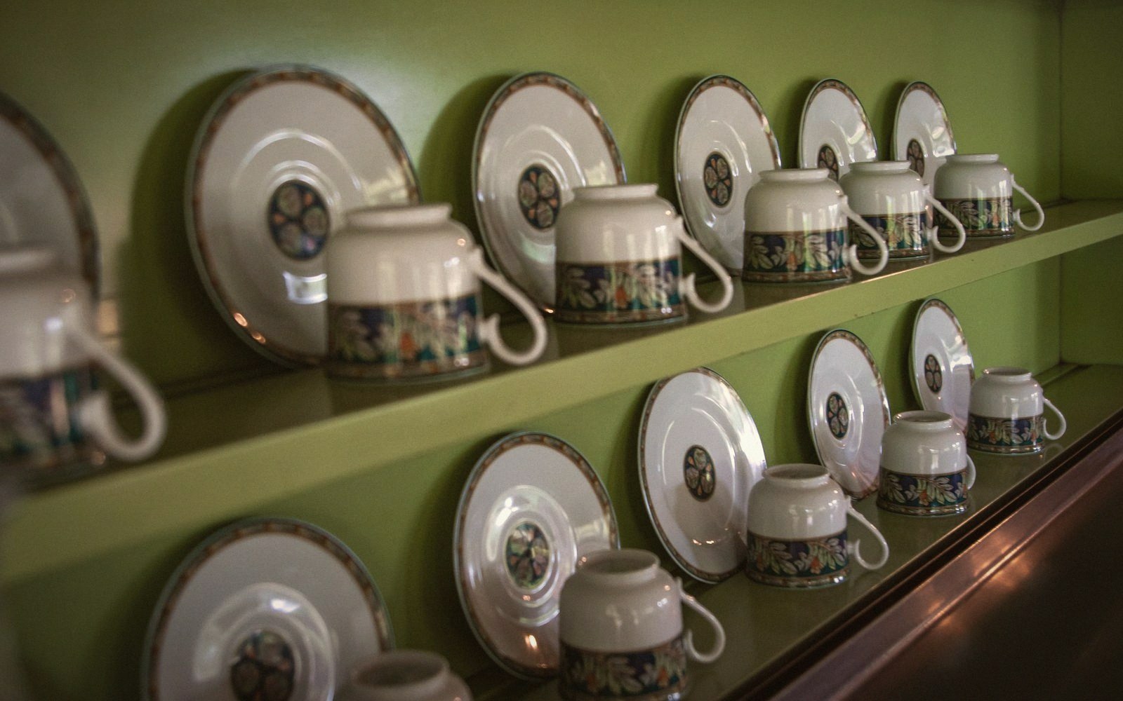 Rows of matching teacups and saucers with floral patterns displayed on green shelves