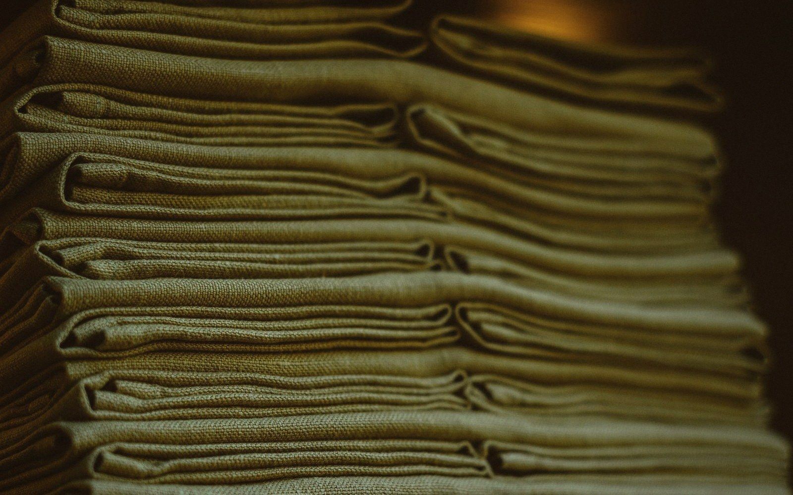 Stacked linen cloths folded into neat layers, viewed close-up in dim light